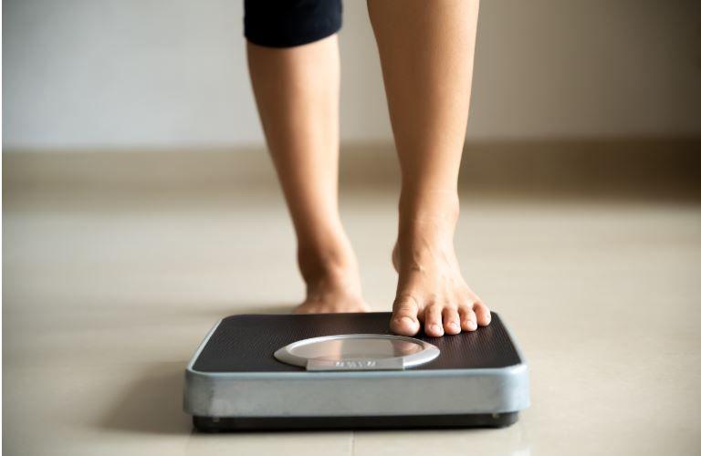 girl stepping on a weight scale, weight loss